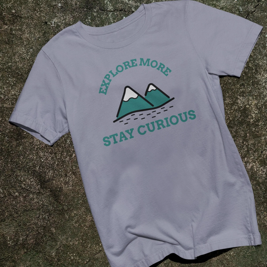Gray t-shirt with 'Explore More, Stay Curious' text and mountain graphic on a stone surface