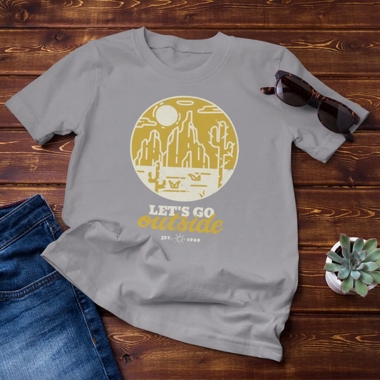 Gray t-shirt with a yellow graphic and text on a wooden surface with jeans and sunglasses.