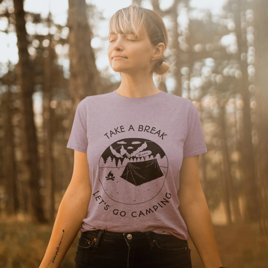 Person wearing a t-shirt with 'Take a Break, Let's Go Camping' design in a forest setting