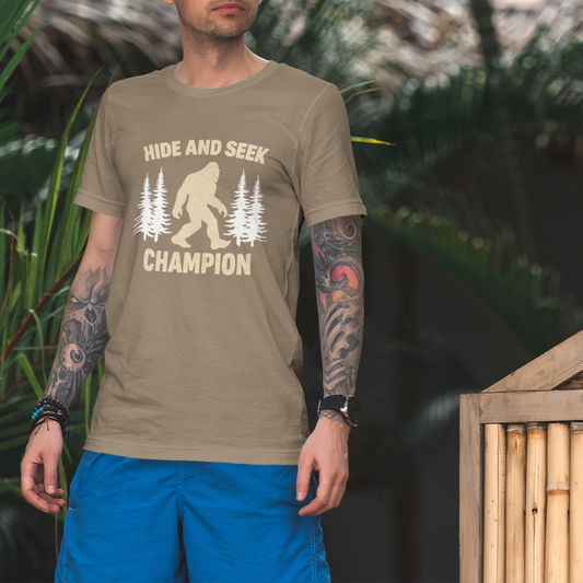 Man wearing a t-shirt with 'Hide and Seek Champion' and a bigfoot graphic outdoors.
