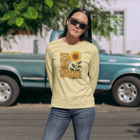 Woman wearing a 'Seek the Sunshine' shirt with a sunflower graphic in front of a green truck.
