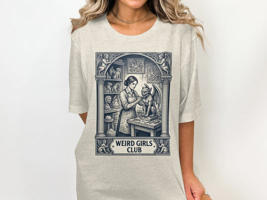 T-shirt with a woman carving a gargoyle in an art studio, "Weird Girls Club" text.
