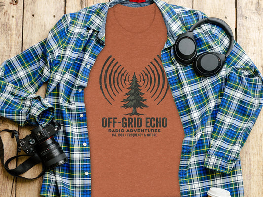 Off-Grid Radio Adventures | Vintage Outdoor Apparel: T-shirt with "OFF-GRID ECHO RADIO ADVENTURES" text, laid on a wooden surface with a camera and headphones.