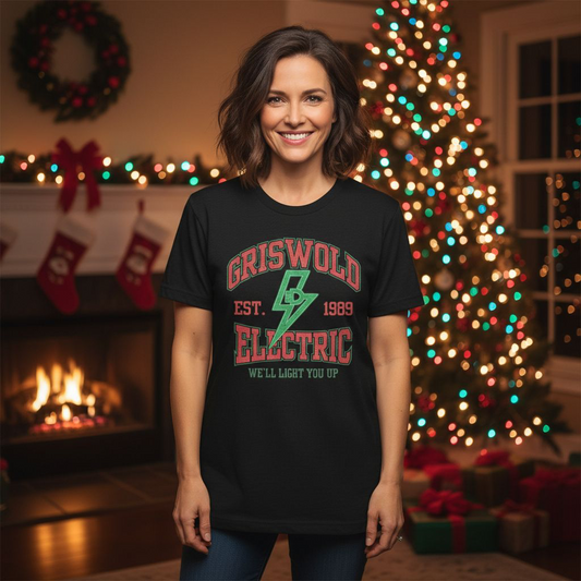 Woman wearing a 'Griswold Electric' shirt in a festive room with Christmas tree and fireplace.