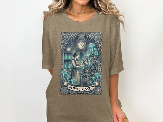 Woman wearing a taupe t-shirt with "Weird Girls Club" text and a fantastical illustration.