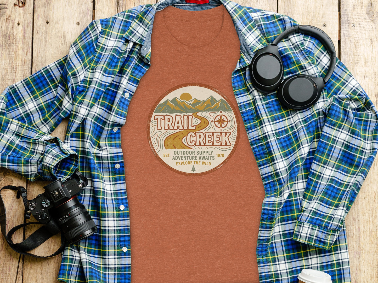 Heritage Heritage Explorer Trail Creek Nomad Tee: Flannel shirt, t-shirt with Trail Creek logo, and headphones on wood.