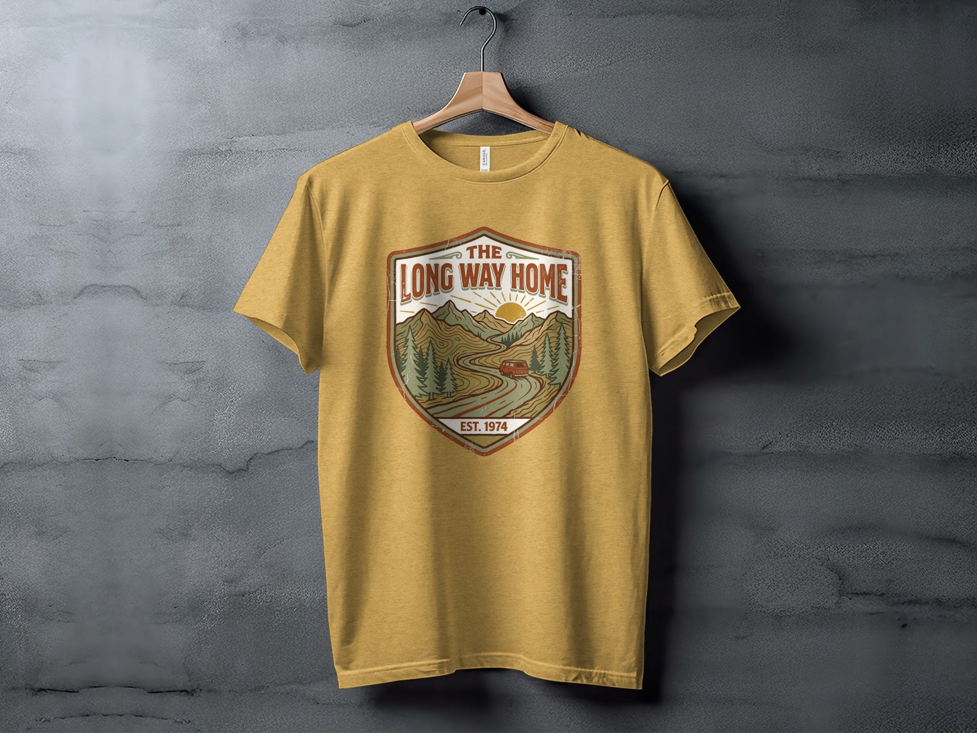 Rugged The Long Way Home | Vintage Adventure Wilderness Shirt: Yellow t-shirt with a shield graphic featuring a scenic mountain road and sun.