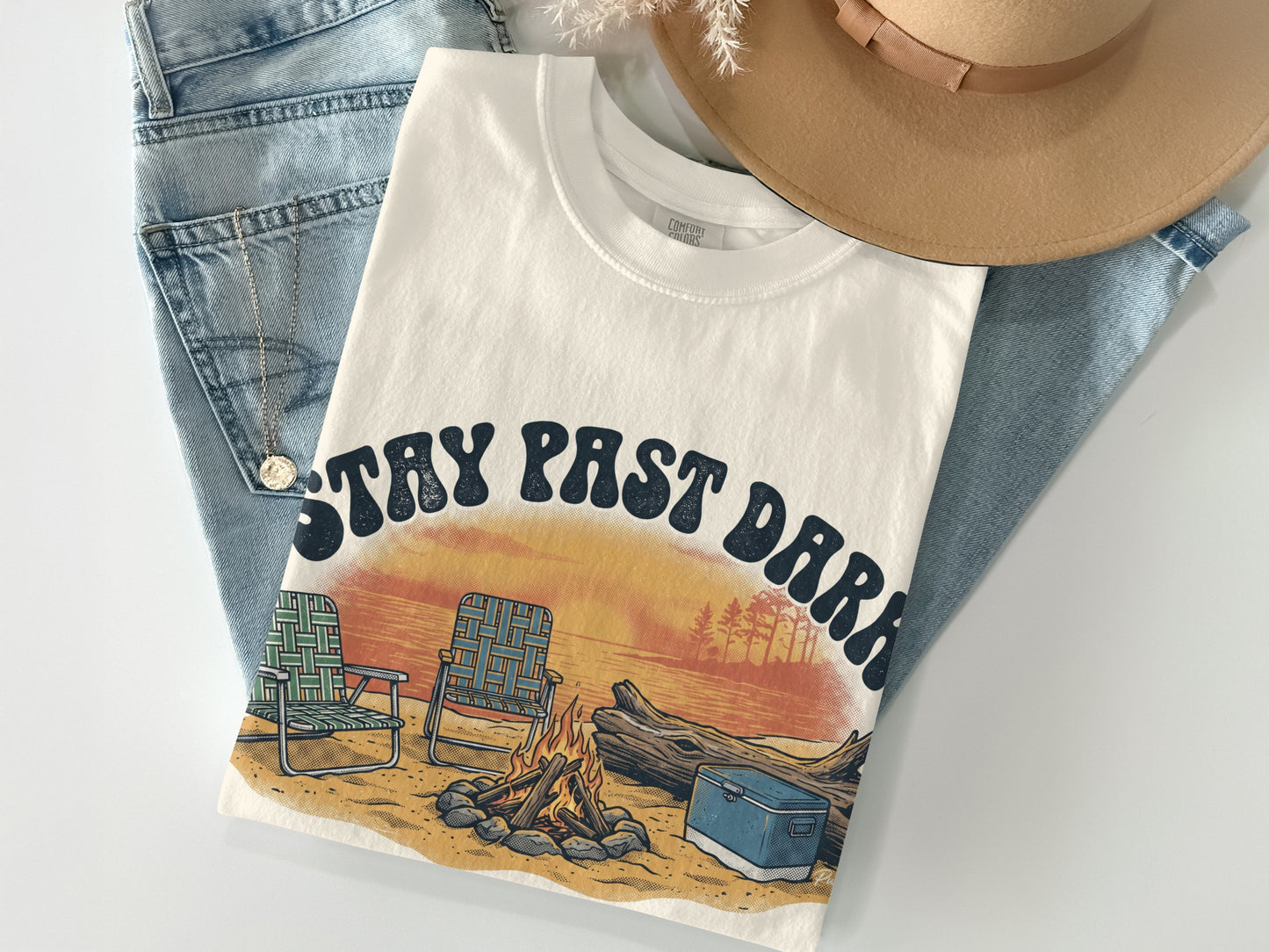 Cream t-shirt with "Stay Past Dark" graphic featuring campfire, chairs, and sunset.