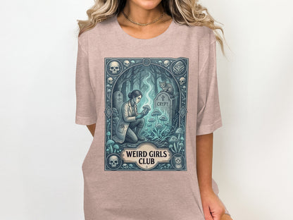 T-shirt graphic of a woman examining mushrooms by a crypt, with skulls and cats.