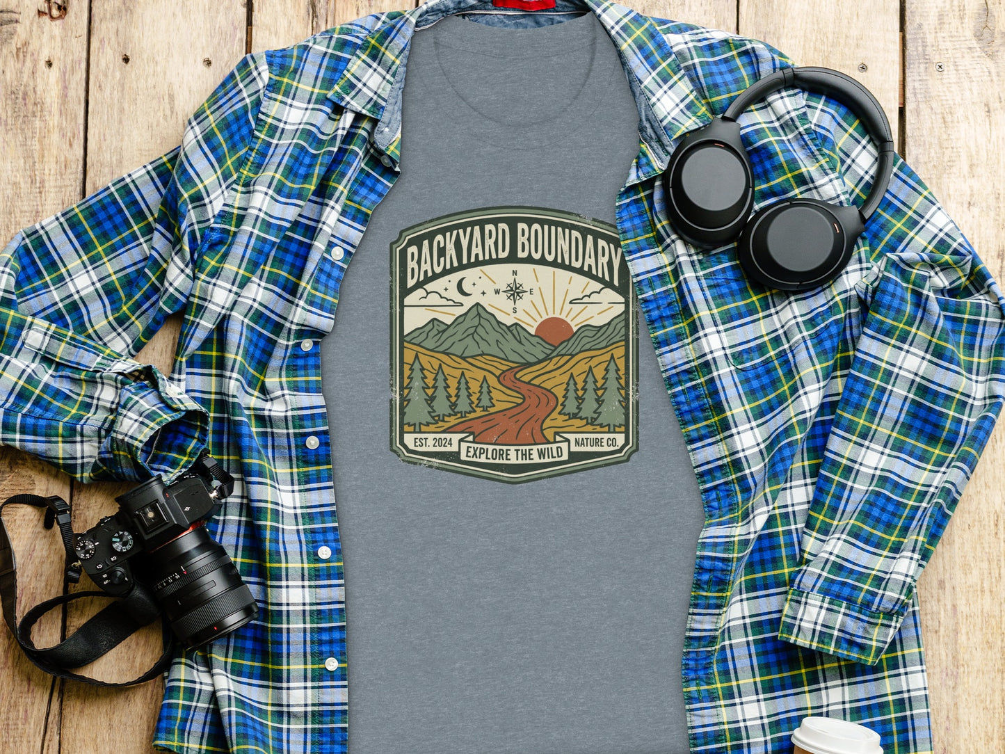Rugged Backyard Boundary: Explore The Wild Wilderness Shirt: Grey t-shirt with "Backyard Boundary" logo, worn over a plaid shirt, with headphones.