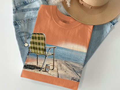 Orange t-shirt with graphic of a chair on a dock by the water.