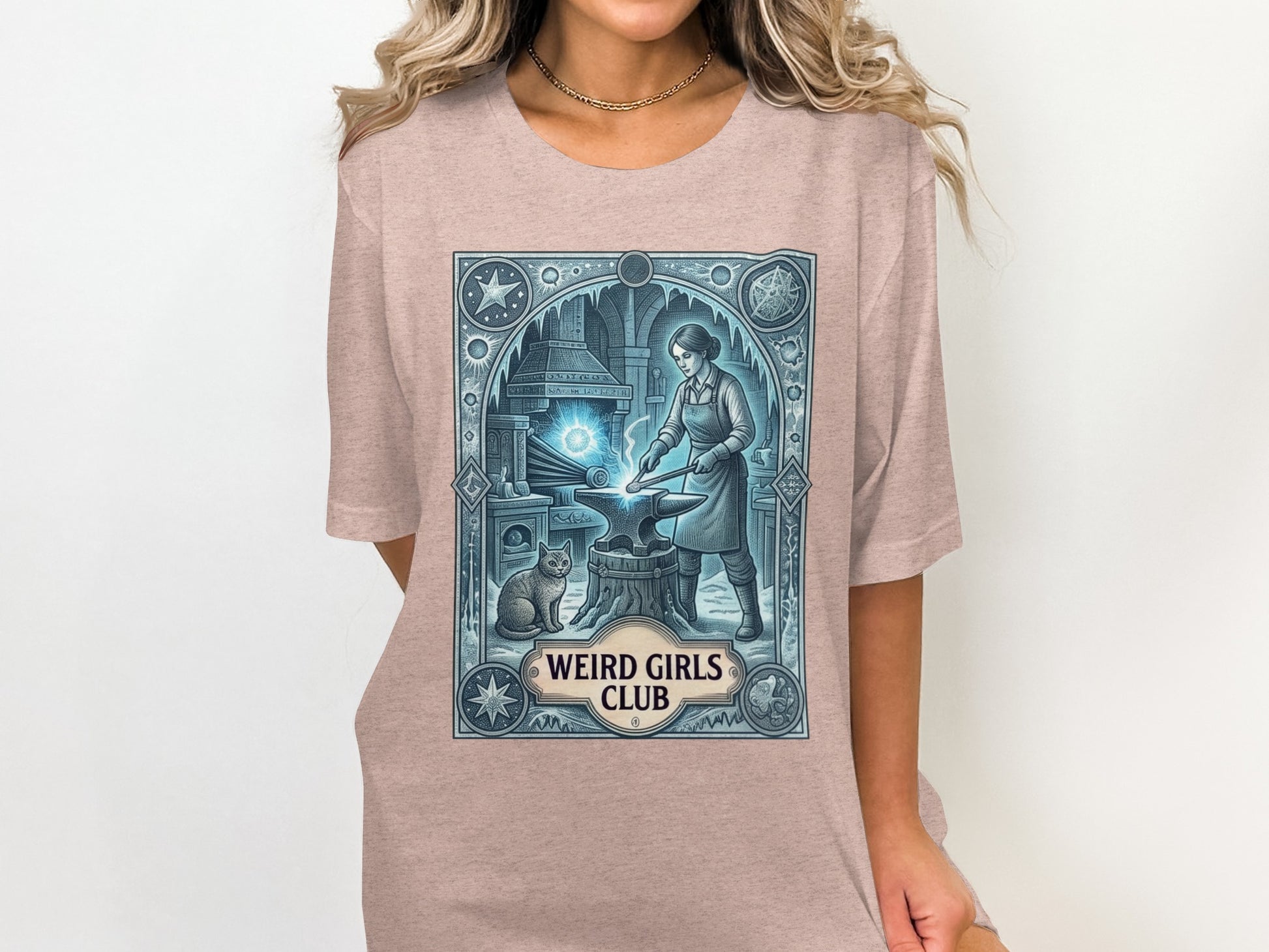 T-shirt graphic of a woman blacksmith and cat in an icy workshop, "Weird Girls Club" text.