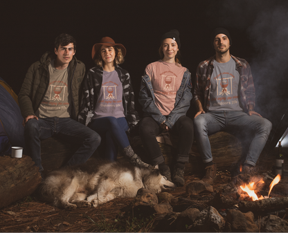 Four people and a dog sitting by a campfire at night with tents in the background.