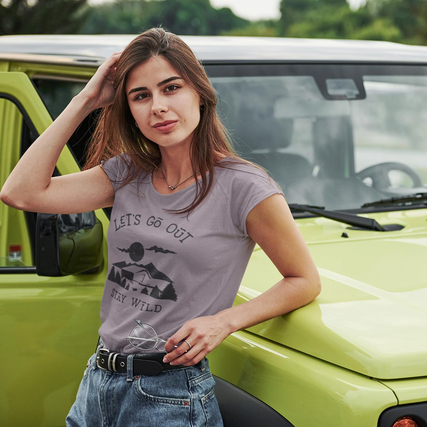 Woman standing next to a green vehicle wearing a t-shirt with text and graphics.