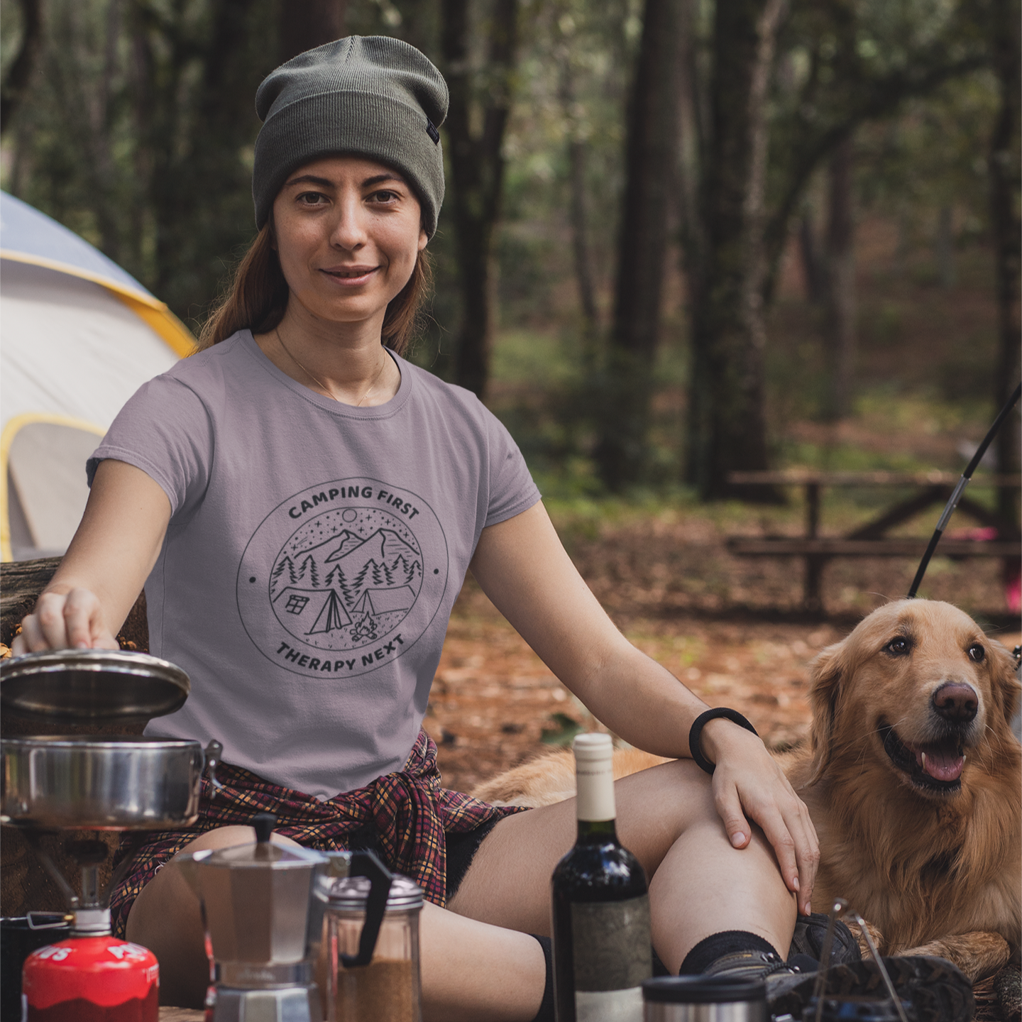 Woman camping with a dog, cooking outdoors in a forest setting