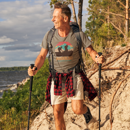 Man hiking on a trail with a backpack and walking sticks, surrounded by trees and water.