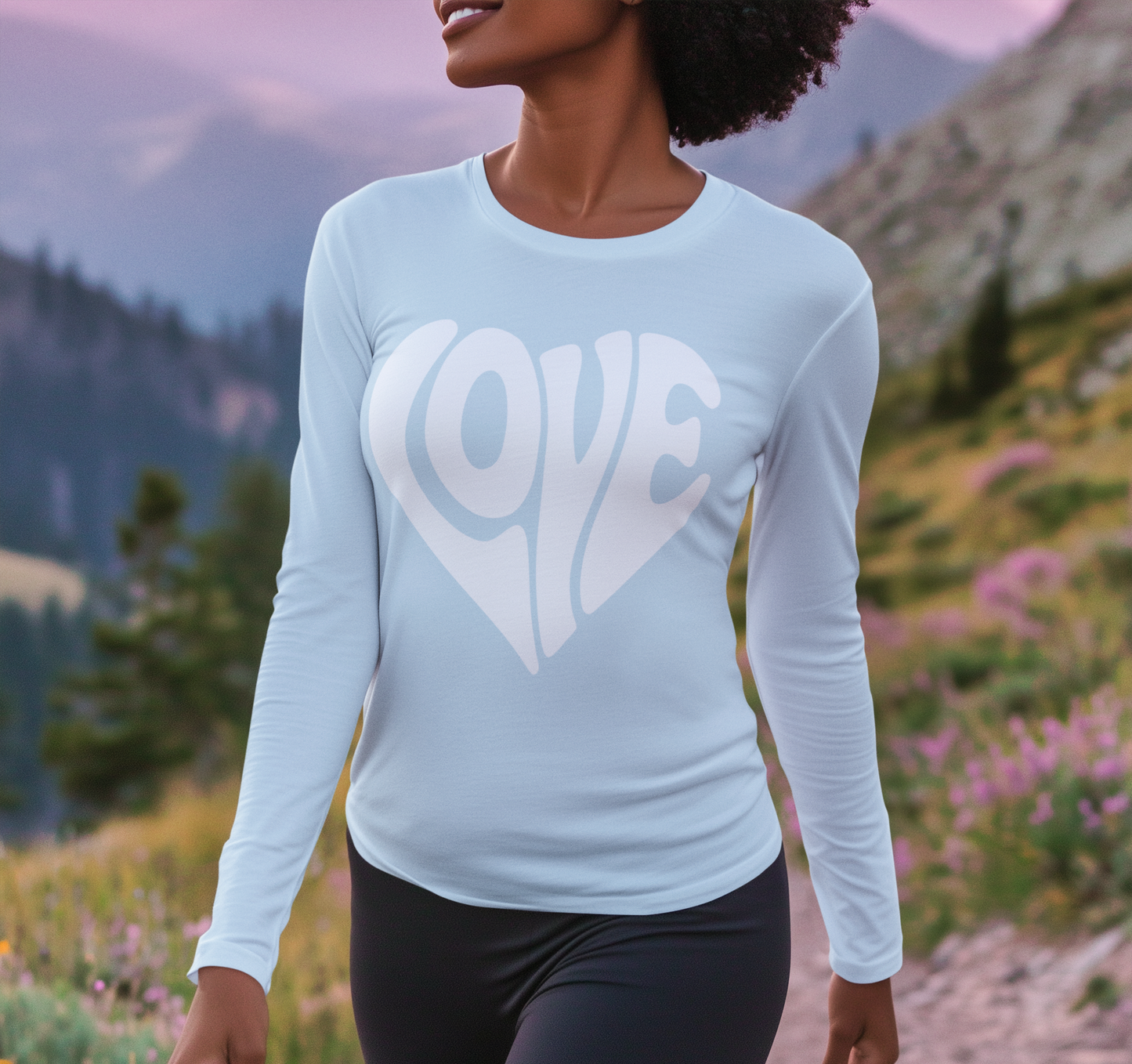 Person wearing a light blue long-sleeve shirt with 'LOVE' printed on it, standing in a mountainous landscape.