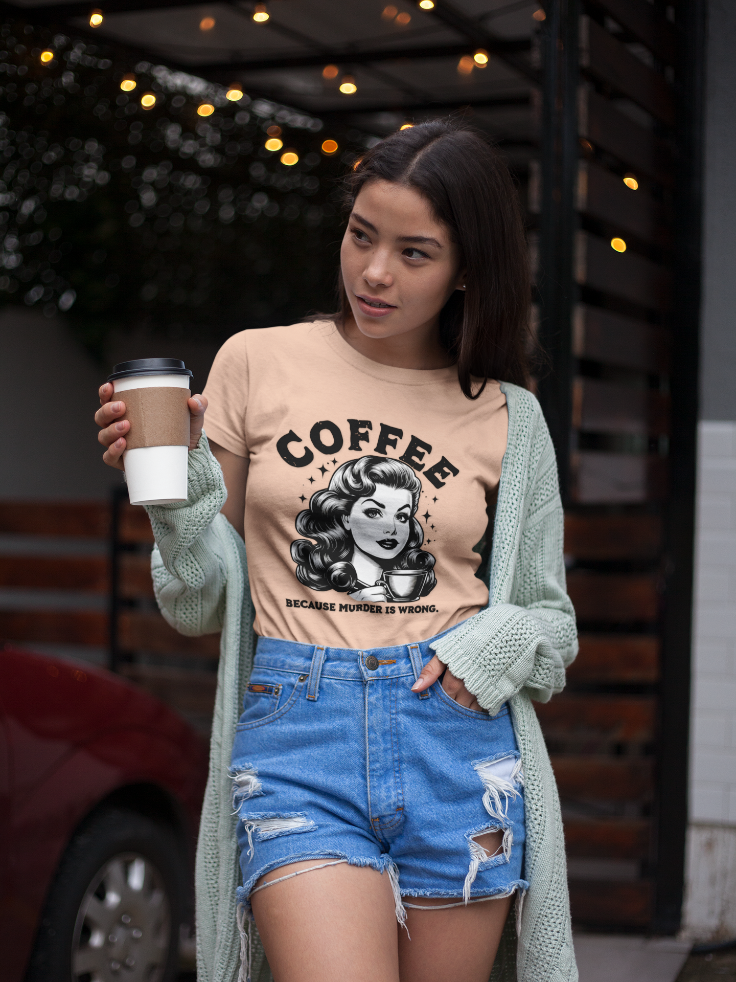 Woman holding a coffee cup wearing a graphic t-shirt with a coffee-themed design.