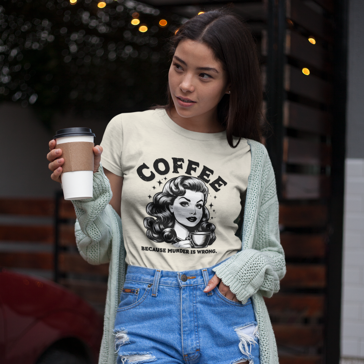 Woman holding a coffee cup wearing a graphic t-shirt with a graphic design and text.