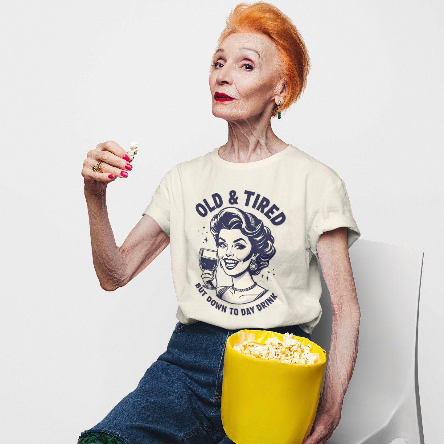 Person wearing a t-shirt with a graphic design, sitting with a popcorn bucket on a white background
