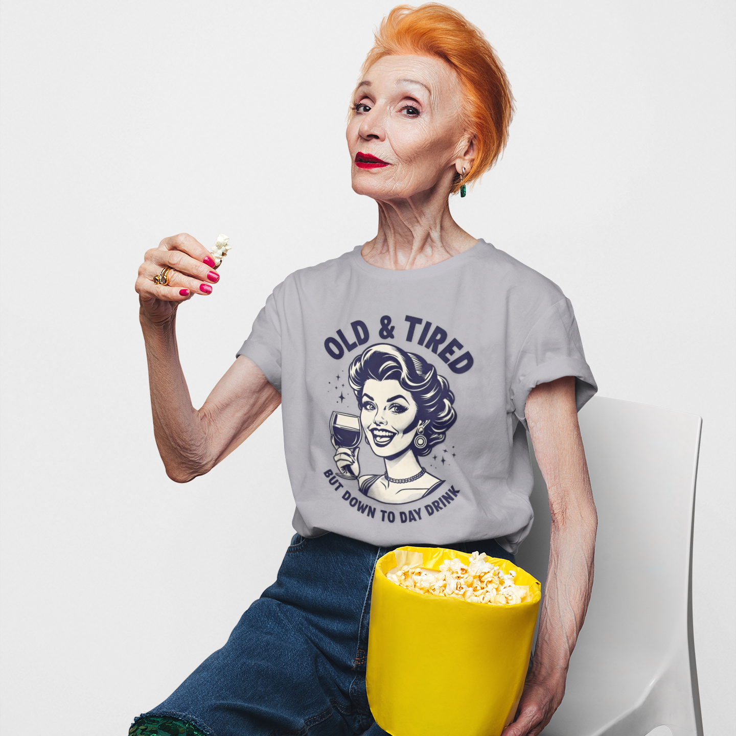 Person wearing a t-shirt with a graphic design, sitting with a bucket of popcorn on a white background