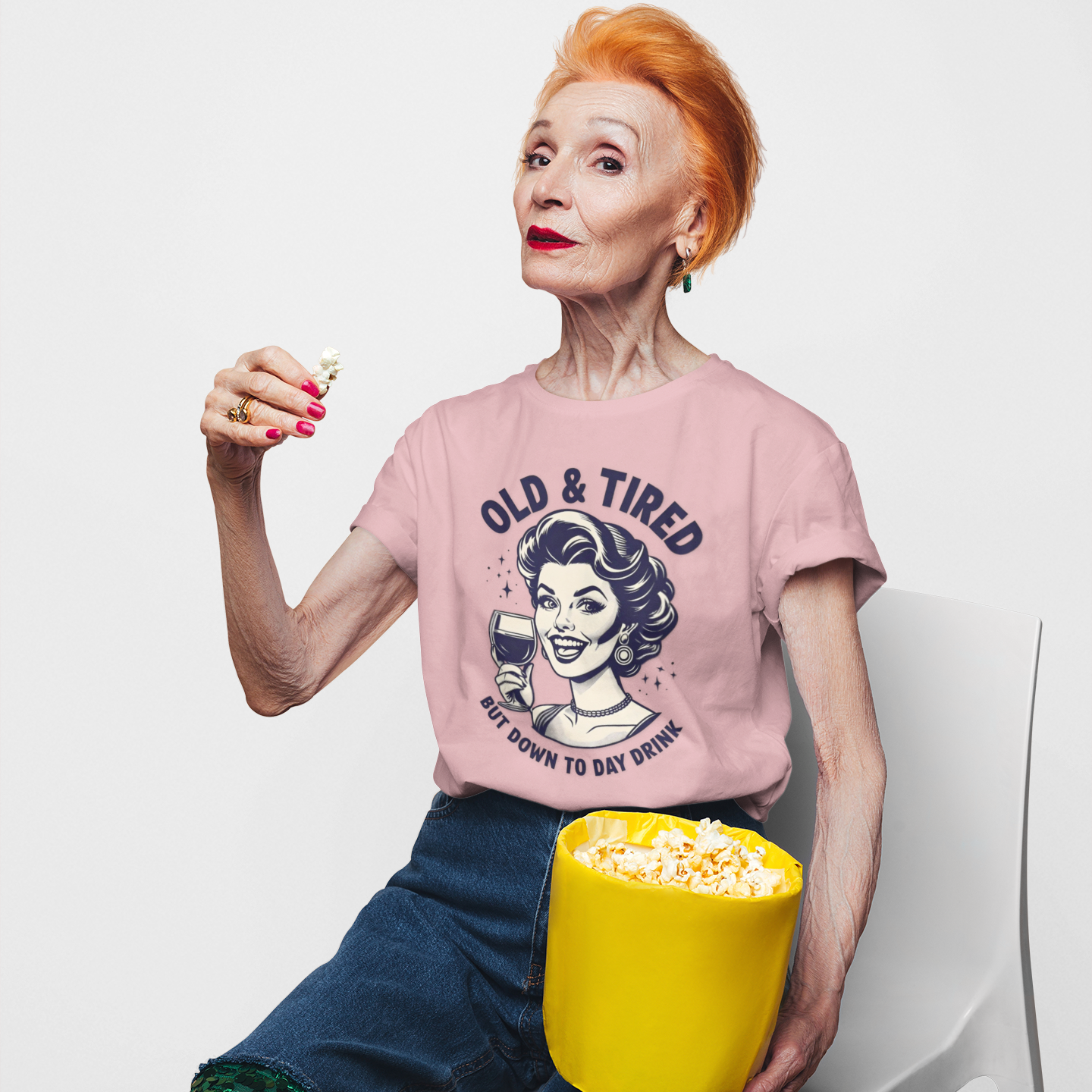 Person wearing a pink t-shirt with a graphic design, sitting with a yellow bucket of popcorn on a white background