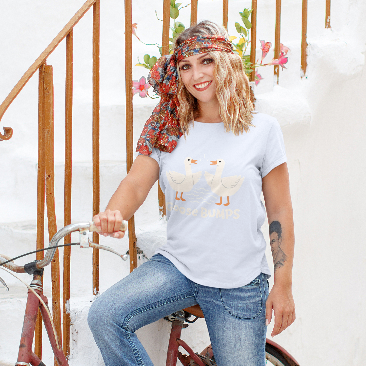 Woman sitting on a bicycle wearing a graphic t-shirt and jeans, with a floral headband and white sneakers.