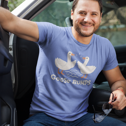 Man sitting in a car wearing a blue t-shirt with a goose graphic and text.