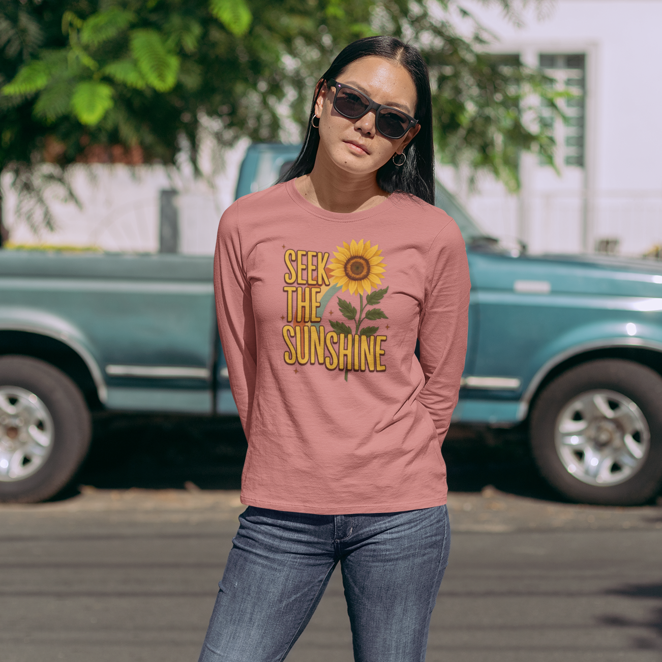 Woman wearing a pink shirt with a sunflower design and text, standing in front of a green truck.