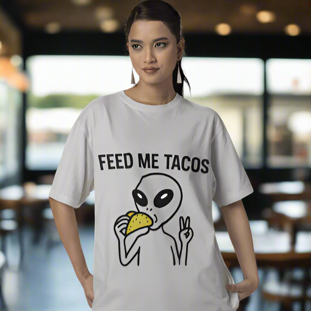 Person wearing a white t-shirt with an alien eating a taco and 'Feed Me Tacos' text.