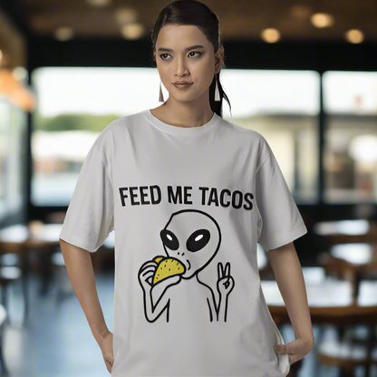 Person wearing a white t-shirt with an alien eating a taco and 'Feed Me Tacos' text.