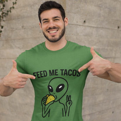 Man wearing a green t-shirt with an alien holding a taco and 'Feed Me Tacos' text, pointing at the shirt.