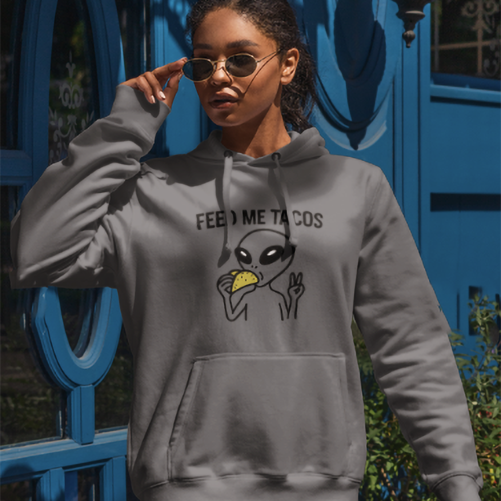 Person wearing a gray hoodie with an alien graphic and text, standing in front of a blue door.