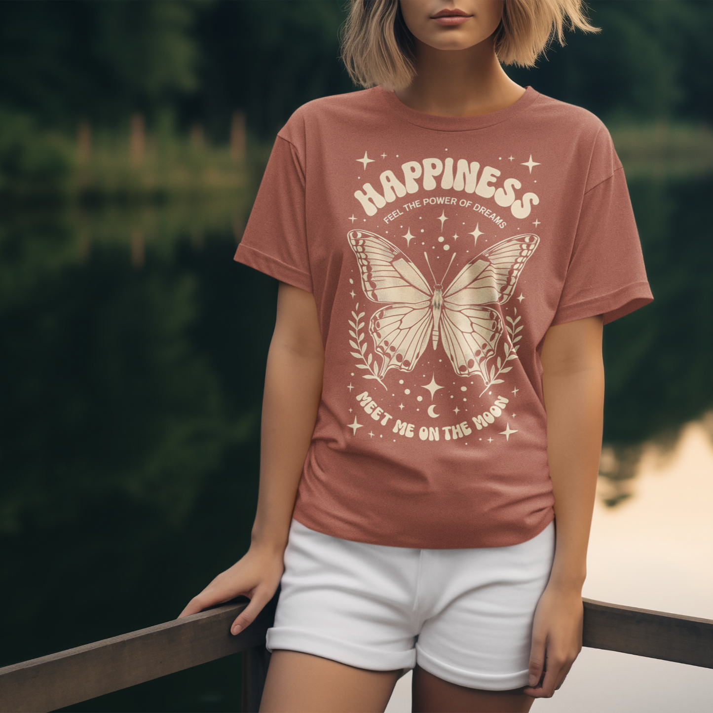 Person wearing a pink t-shirt with a butterfly design and 'Happiness' text, standing by a lake.