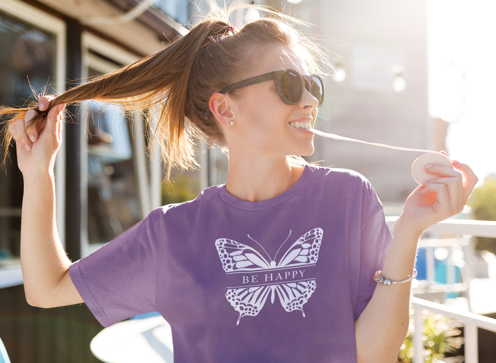Woman wearing a purple t-shirt with a butterfly design and 'BE HAPPY' text, outdoors.