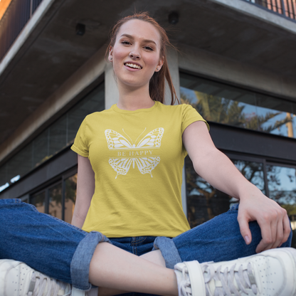 Woman sitting on a ledge wearing a yellow t-shirt with a butterfly design, in front of a modern building.