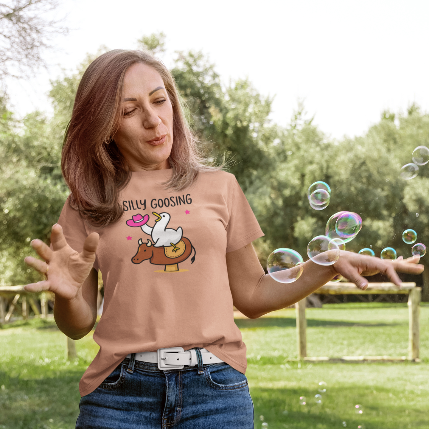 Woman blowing bubbles outdoors wearing a t-shirt with a graphic design.