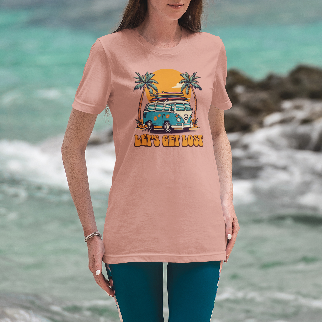 Person wearing a pink t-shirt with a graphic design of a van and palm trees, standing by a rocky coastline.