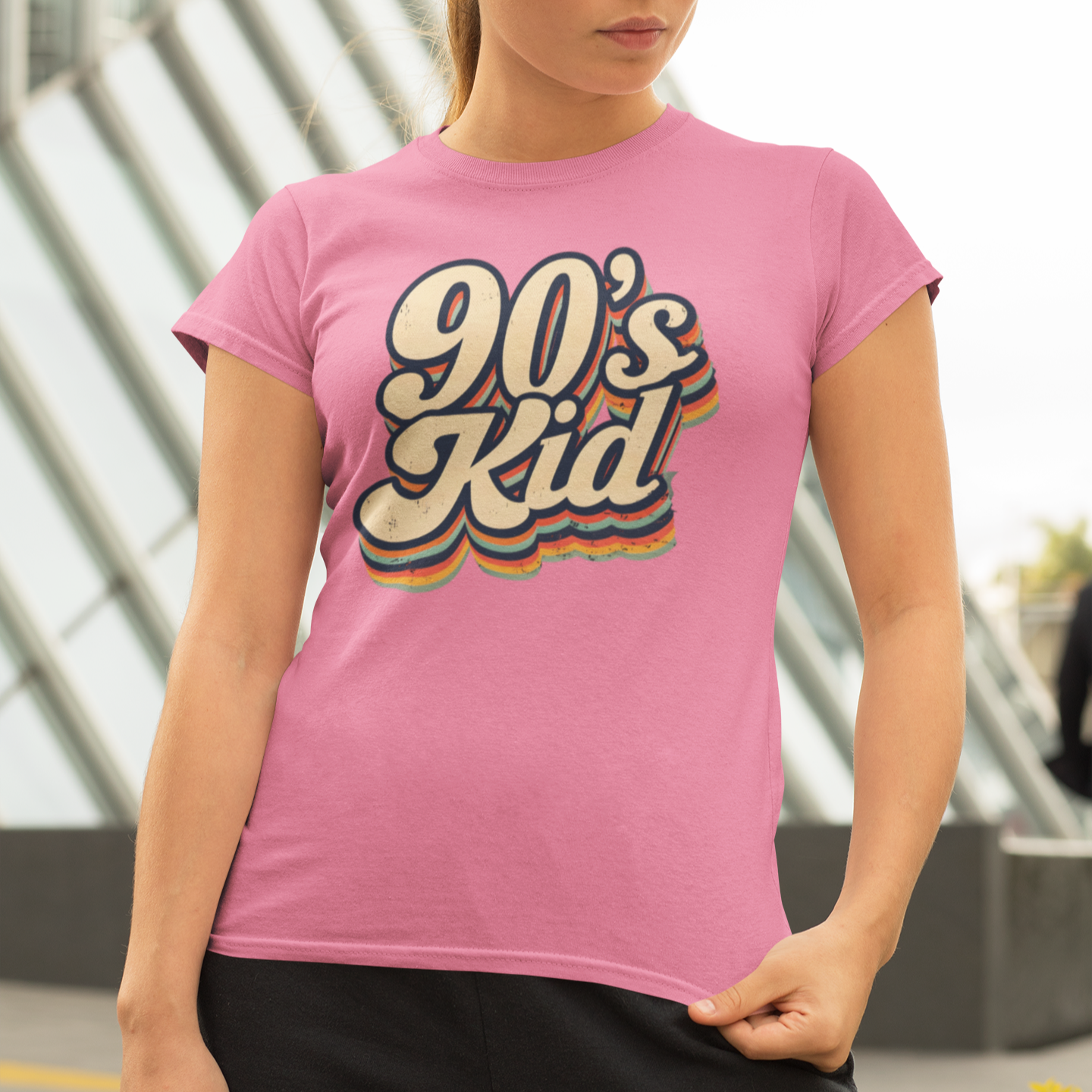 Woman wearing a pink t-shirt with '90's Kid' design outdoors.