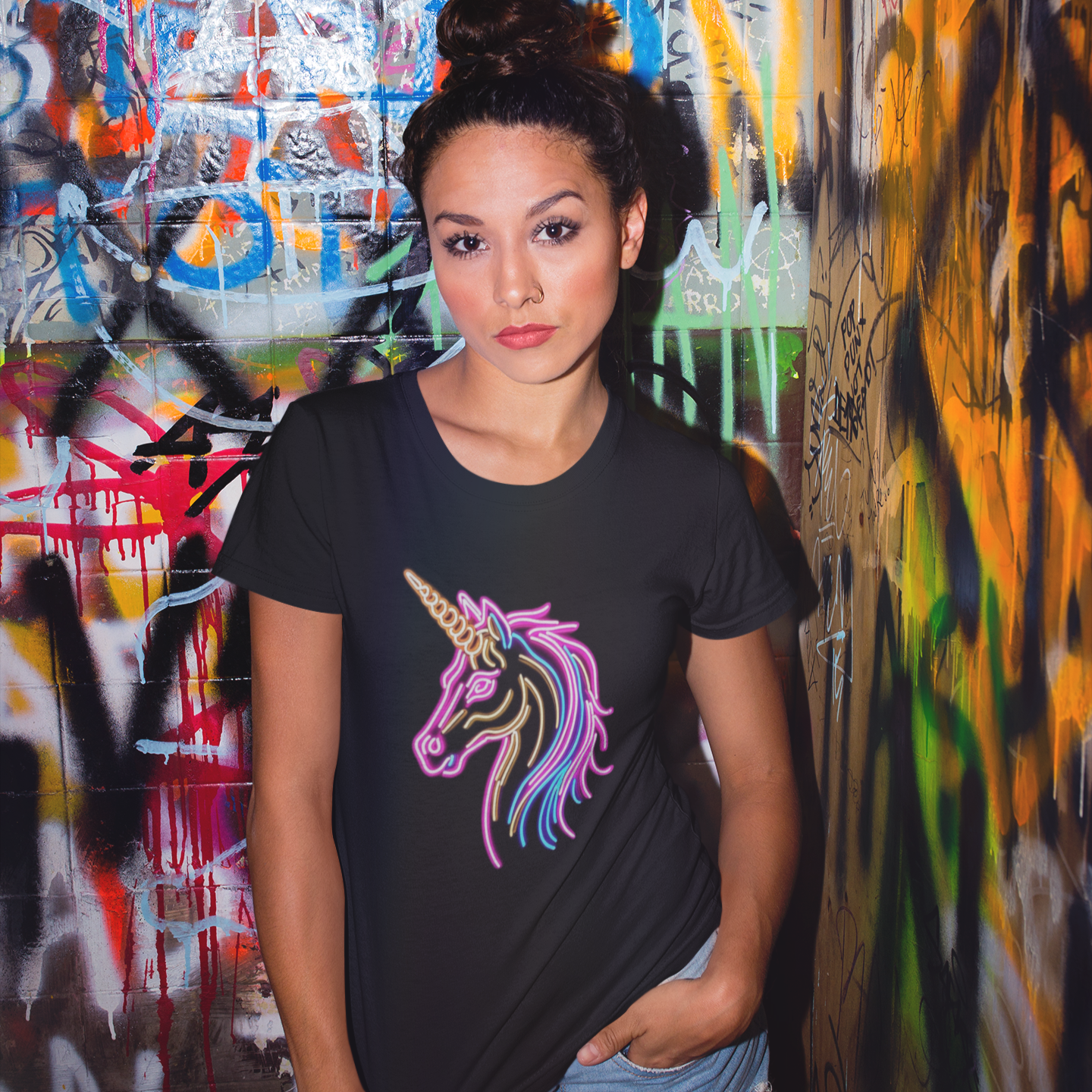 Woman wearing a black t-shirt with a colorful unicorn design in front of a graffiti-covered wall.