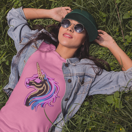Woman wearing a pink shirt with a unicorn design, denim jacket, and green hat lying on grass.