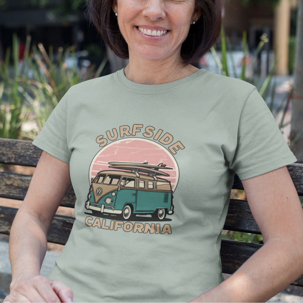 Woman wearing a 'Surfside California' t-shirt with a vintage van design, sitting on a bench outdoors.
