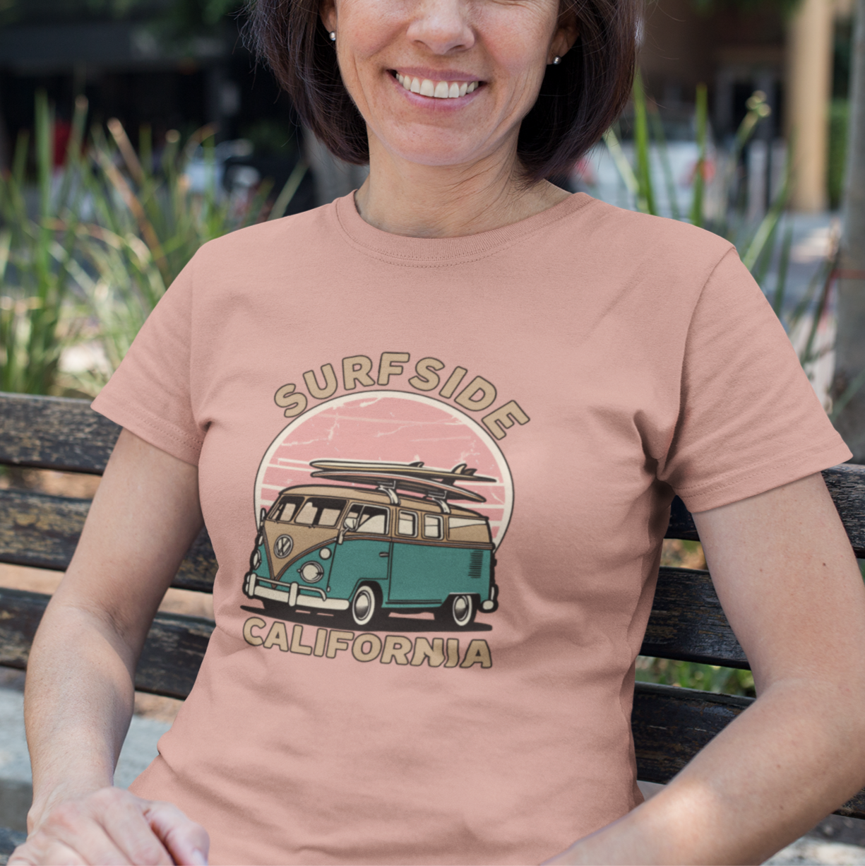 Woman wearing a 'Surfside California' t-shirt with a van graphic, sitting on a bench outdoors.