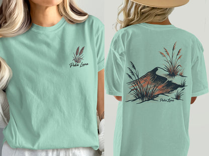 Mint green t-shirt with Puka Luna logo and rust-colored bird and grass design.