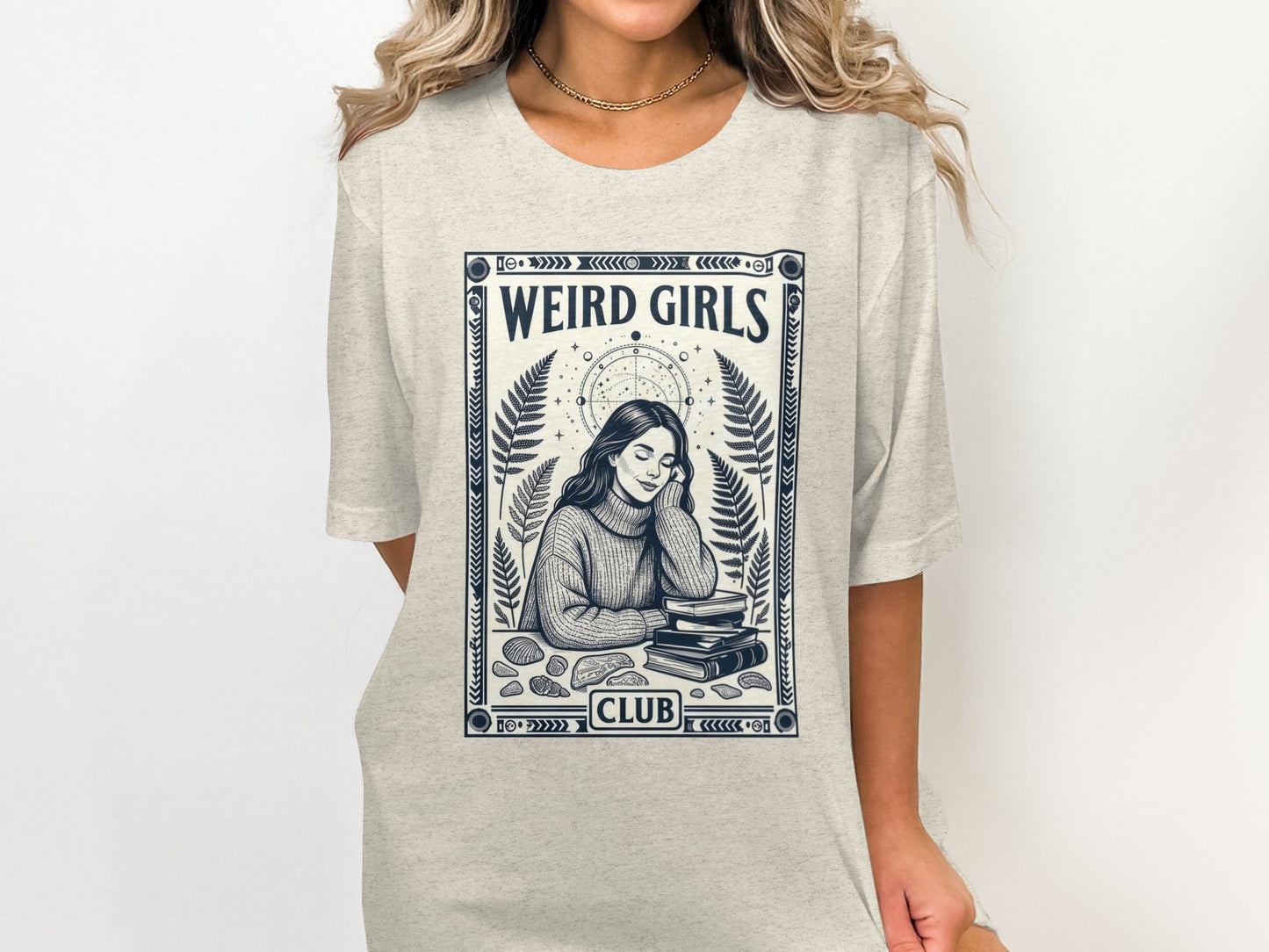 T-shirt featuring "Weird Girls Club" text and illustrations of books and celestial elements.