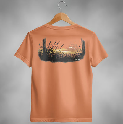 Orange t-shirt with a painting of a boat at sunset behind tall grass.