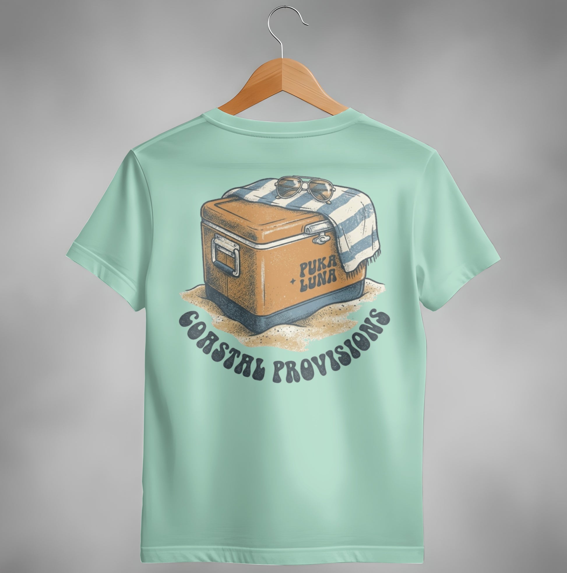 Cooler with towel and sunglasses on sand, "Puka Luna Coastal Provisions" text.