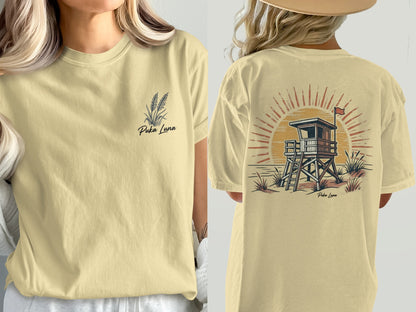 Two views of a light yellow t-shirt with Puka Luna text and a sunset lifeguard stand design.