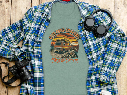 Heritage Dirt Road Graduate Adventure Tee Nomad Tee: T-shirt with "Dirt Road Graduate Take The Detour" text and van graphic, flat lay with camera and headphones.
