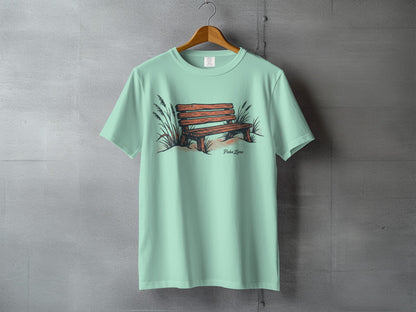 Mint green t-shirt with a drawing of a wooden bench and tall grass.